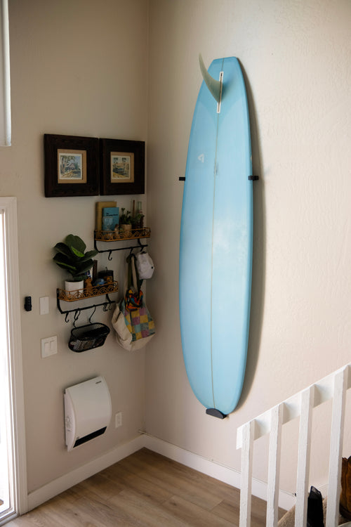 Longboard surfboard mounted vertically on a white wall using TrueRack surfboard mount.