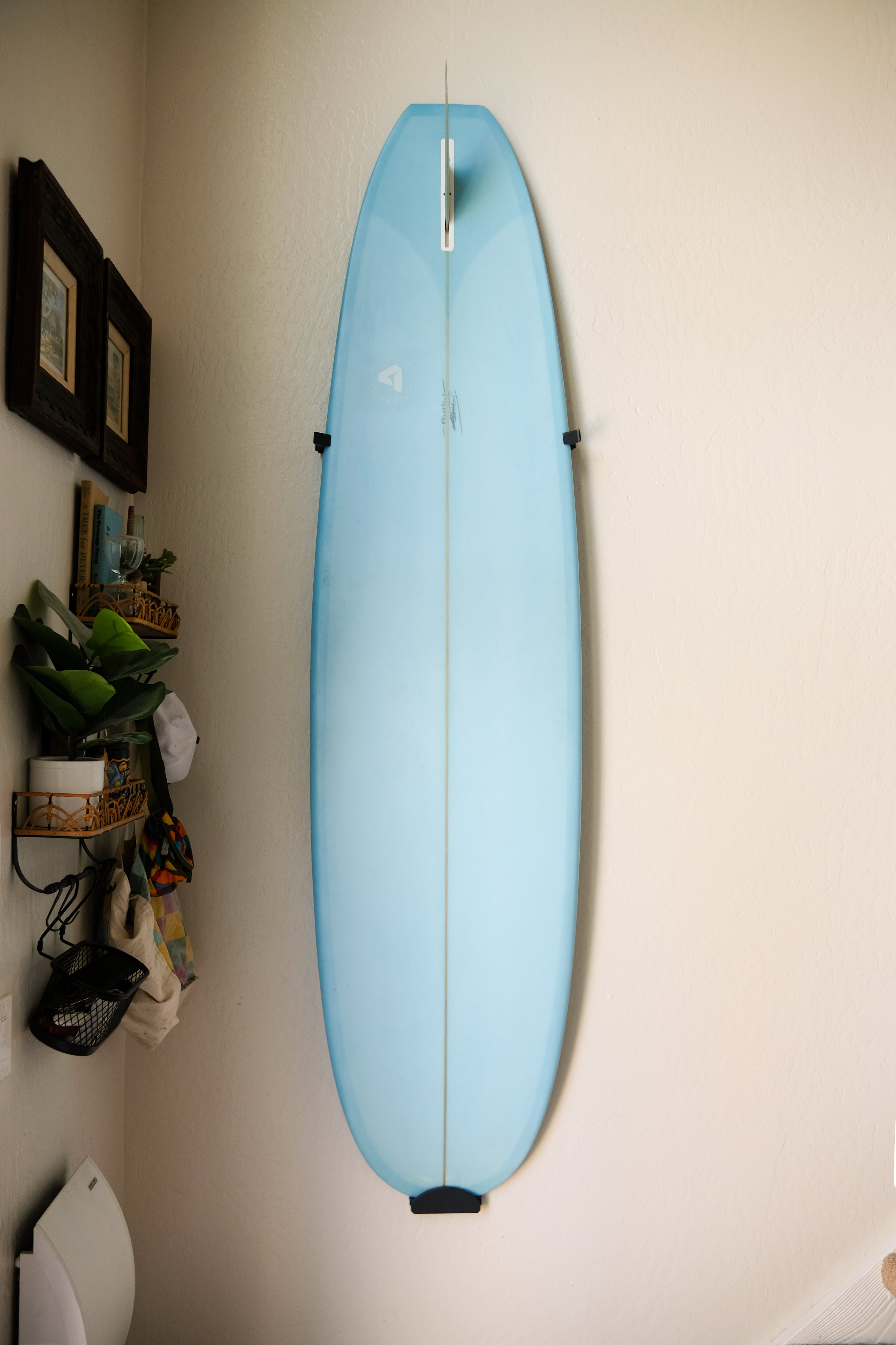 Longboard surfboard mounted vertically on a white wall using TrueRack surfboard mount. Straight on.