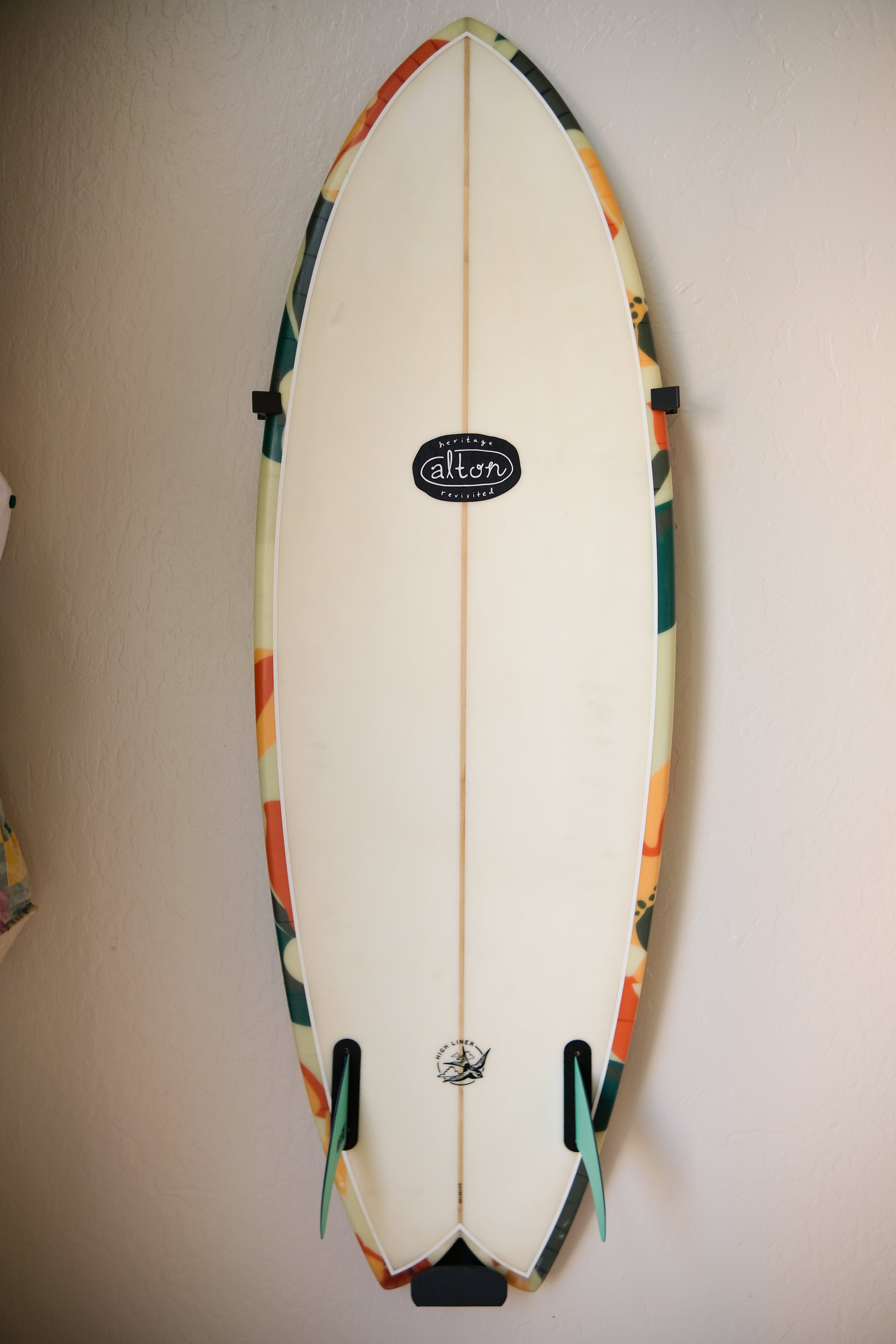 Fish surfboard mounted on an indoor wall using TrueRack surfboard mount, shown in a bright interior setting. Straight on.