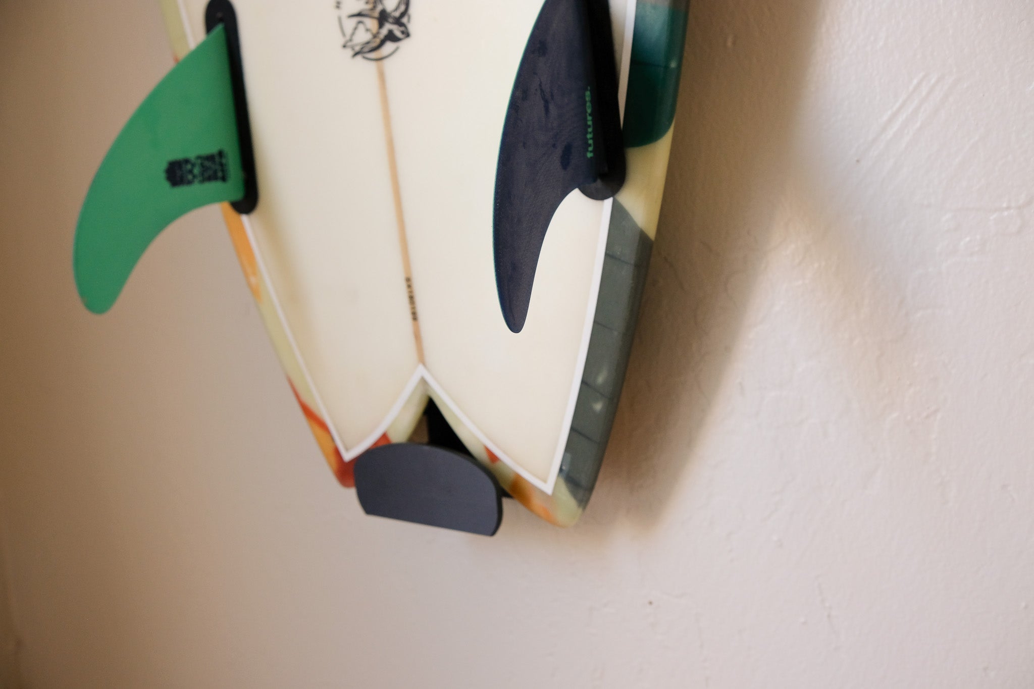 Fish surfboard mounted on an indoor wall using TrueRack surfboard mount, shown in a bright interior setting. Close up Base.