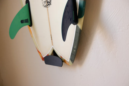 Fish surfboard mounted on an indoor wall using TrueRack surfboard mount, shown in a bright interior setting. Close up Base.