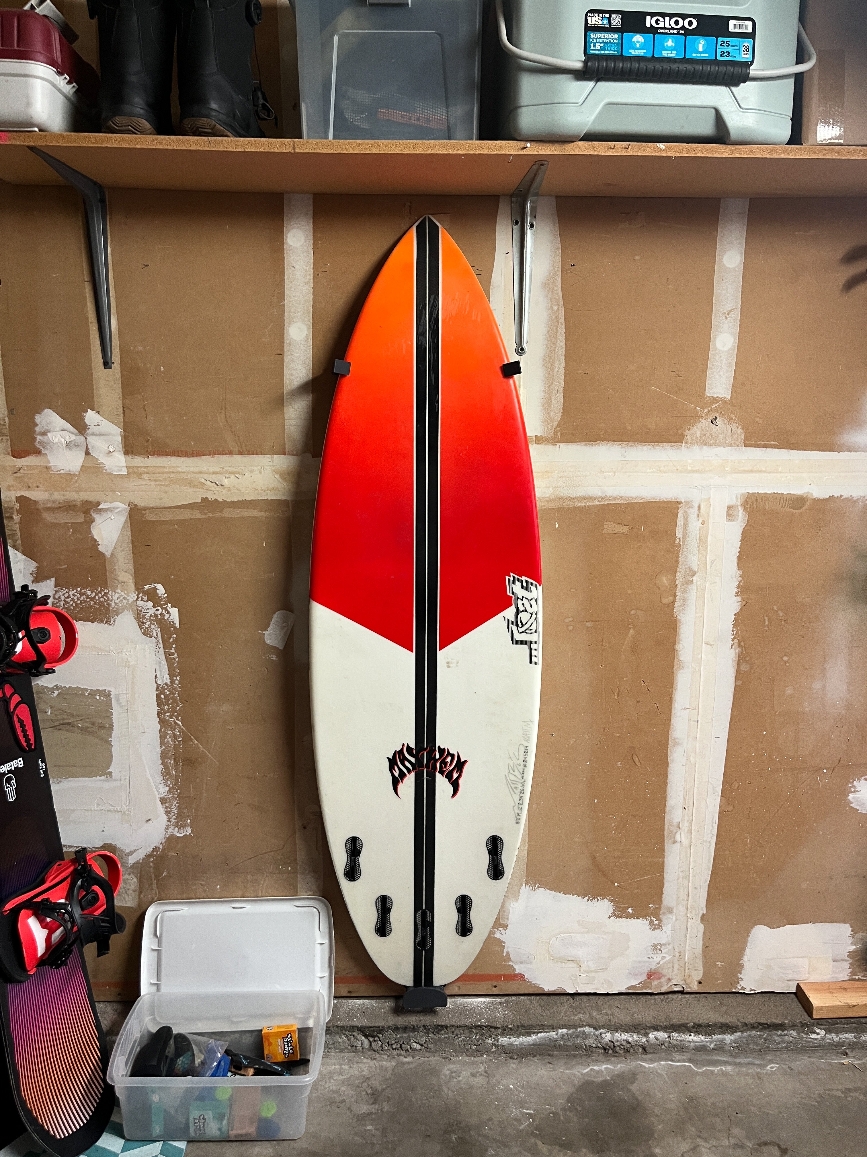 Shortboard surfboard secured on a garage wall with TrueRack surfboard mount, near garage storage shelves.